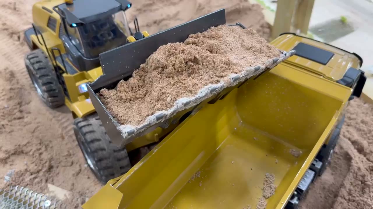 RC loader tipping sand into a dump truck at Crawler World Construction Works